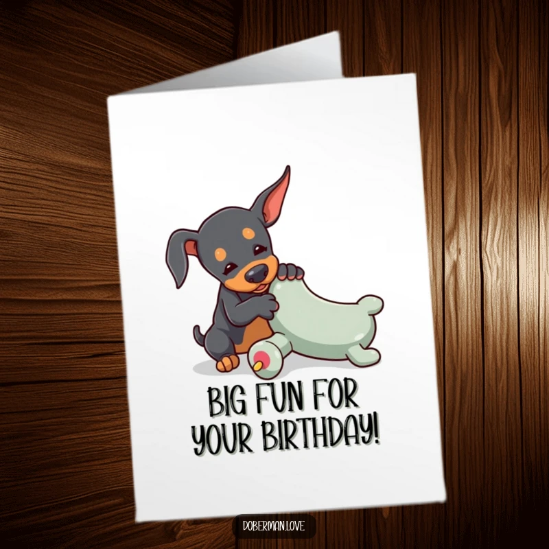 Free Printable Birthday Card: A tiny Doberman playfully wrestles with a comically oversized toy chew, a birthday surprise.