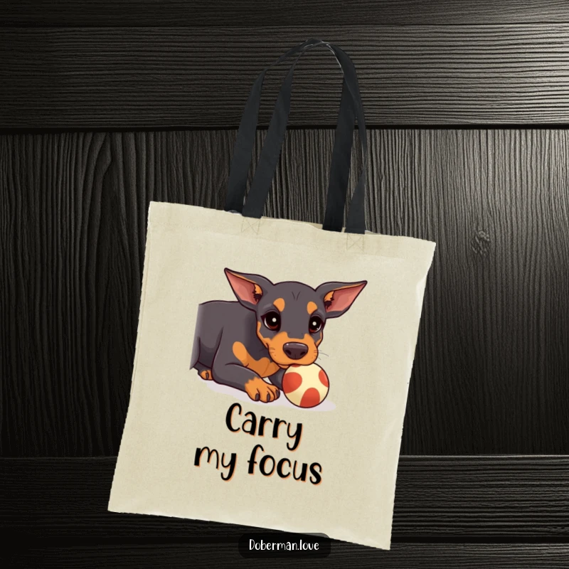 Funny Doberman Tote Bag showcasing a kawaii doberman puppy intently trying to balance a small ball on its nose.